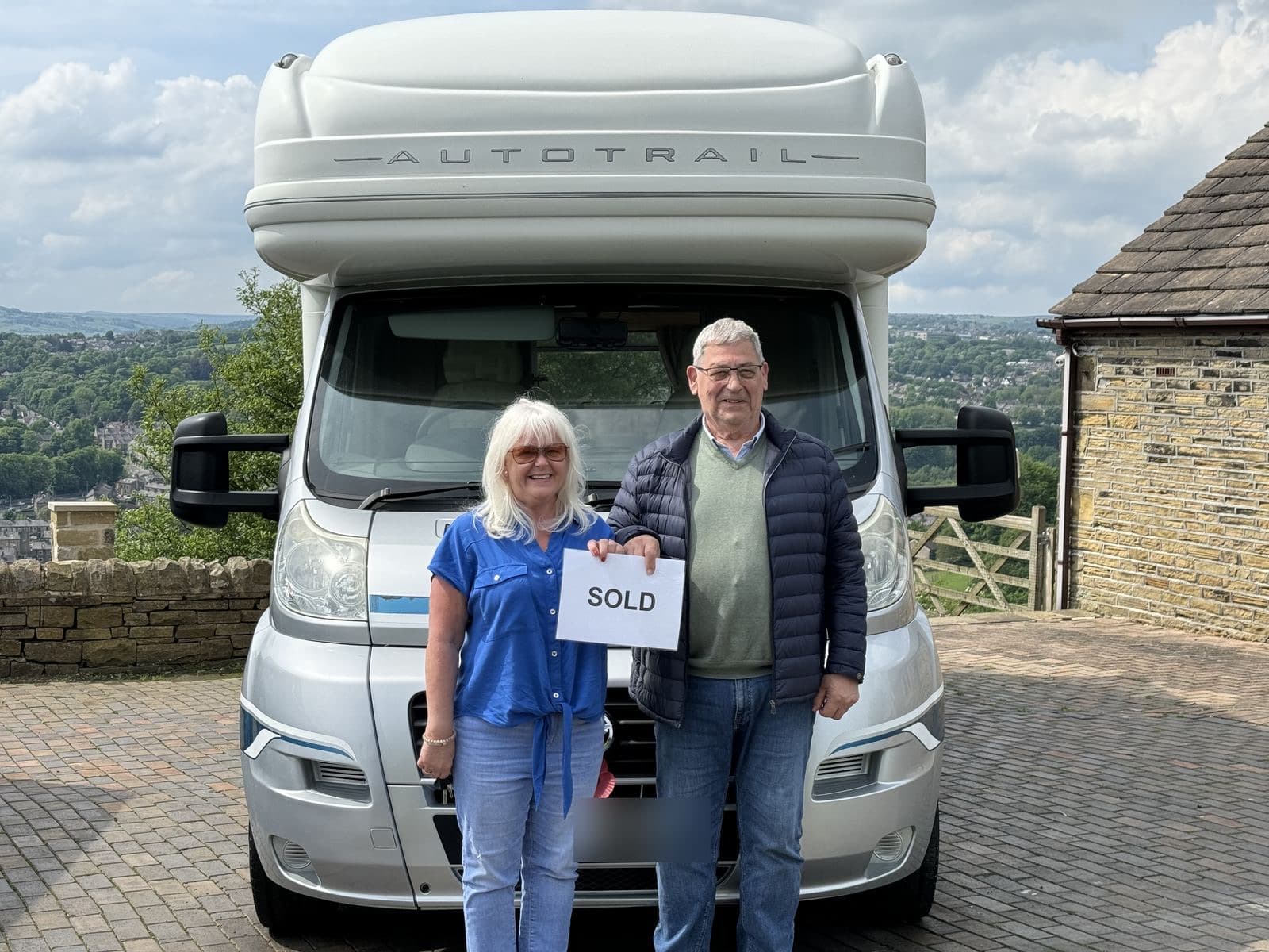 A couple holding a SOLD sign in front of their Auto-Trail motorhome on a bright summer day above the Calder Valley